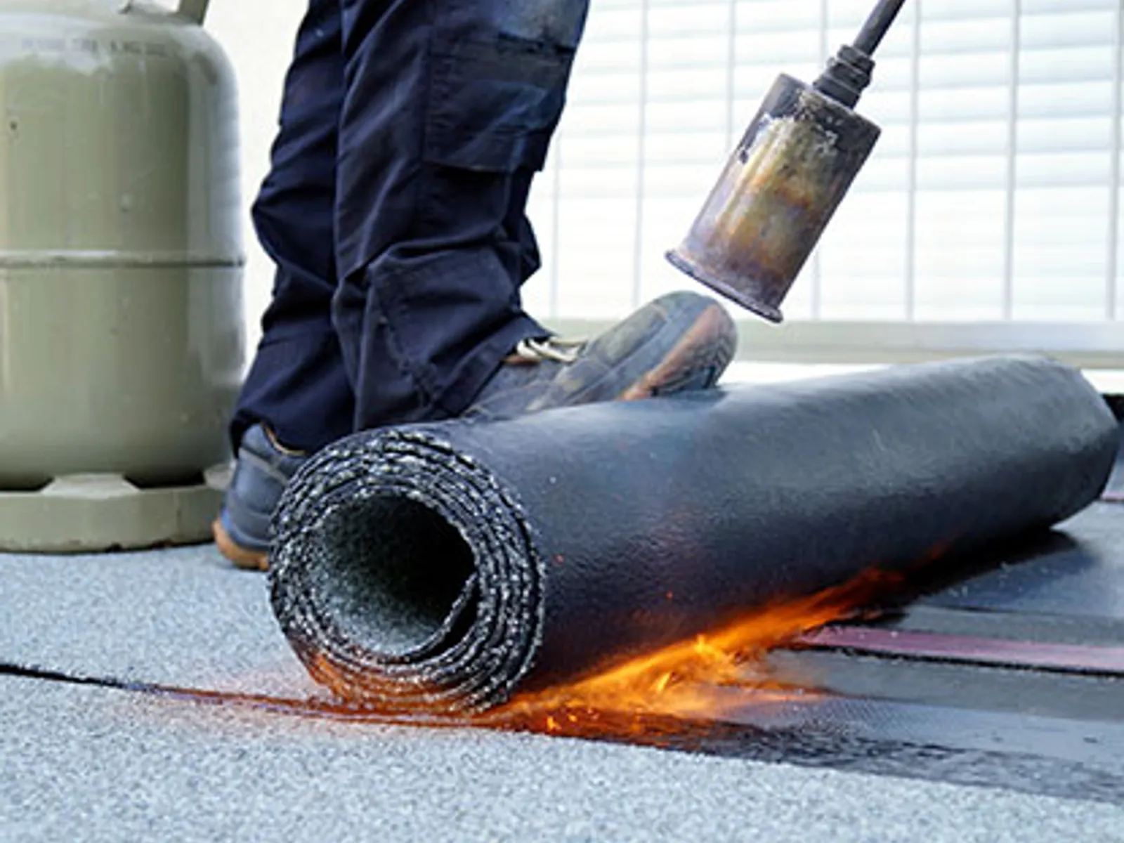 Roofer torch-applying a modified bitumen membrane during a commercial roof replacement