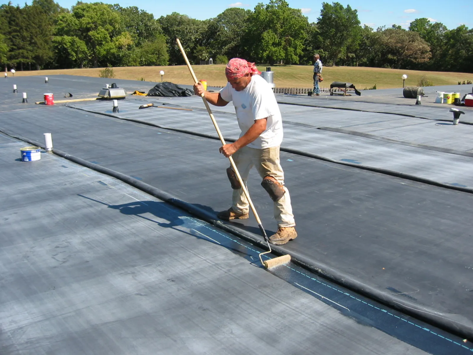 Roofer applying adhesive to a black EPDM membrane roof