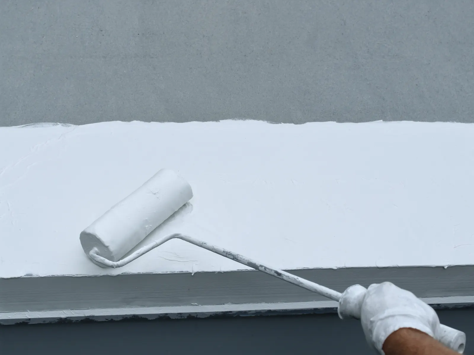 Roller applying bright white silicone coating on a commercial roof