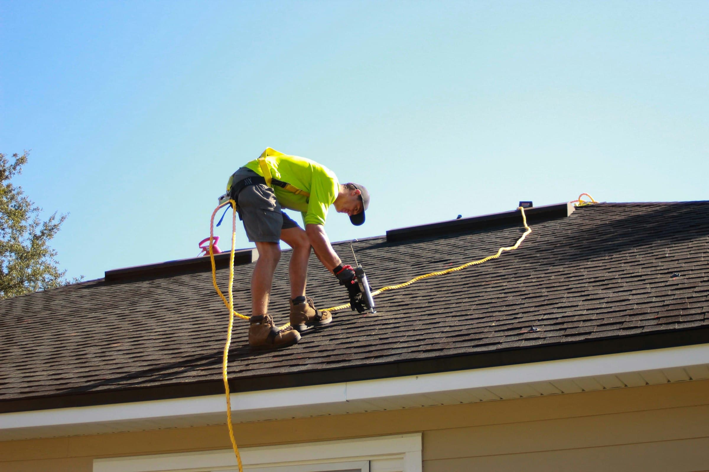 Roofer in a safety harness installing asphalt shingles on a residential roof