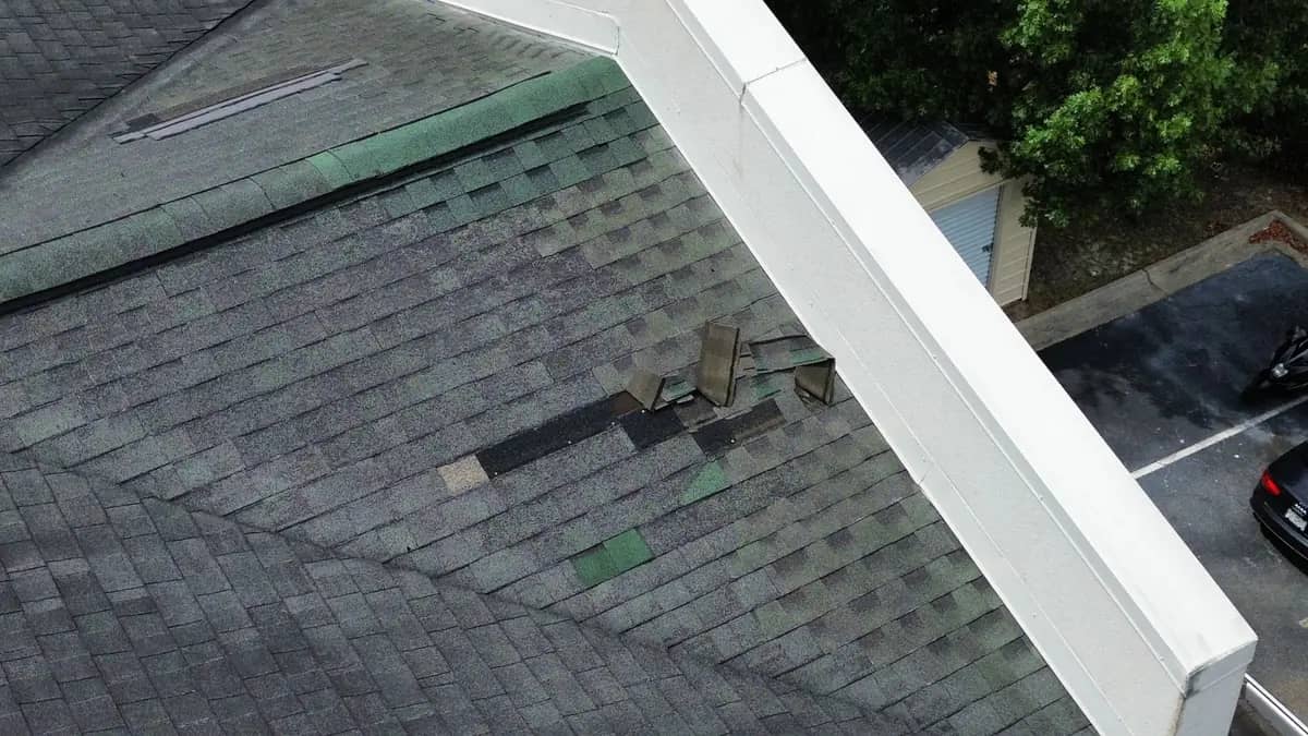 Torn shingles beside a roof penetration, with the layer beneath showing through